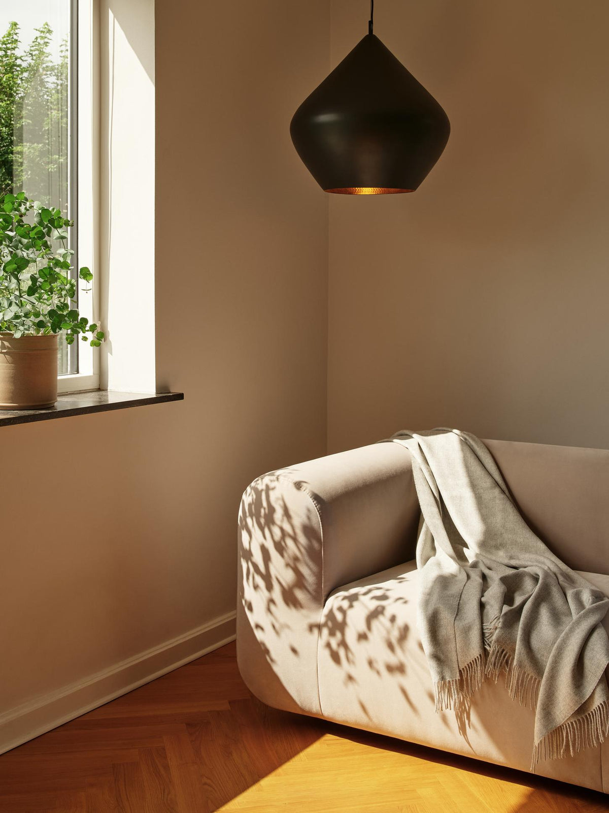 Tom Dixon Beat Fat Pendant in Matt Black Brass above a lounge chair